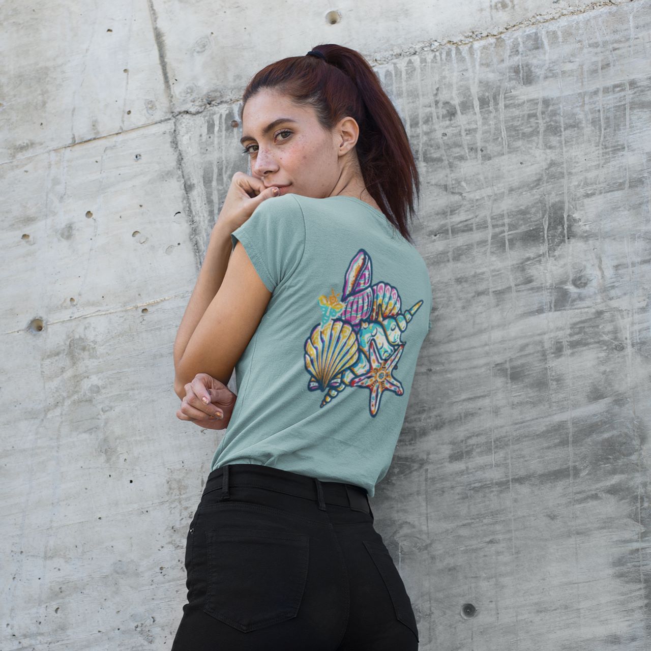 Back view of a woman wearing a sage-green t-shirt with a colorful seashell and starfish illustration, featured in image_4e60fe.jpg.